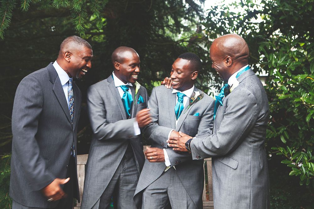 Four groomsmen in gray suits with teal ties laughing together outdoors at a wedding celebration. At Oaks farm wedding venue in Surrey