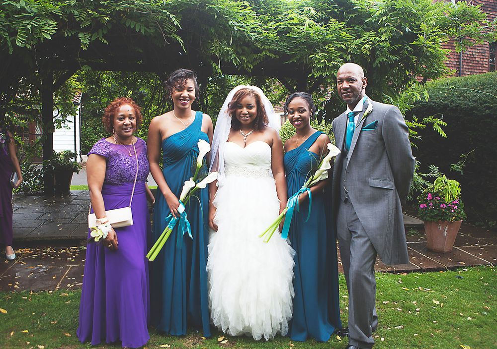 Bride in white gown poses with bridesmaids in teal and purple dresses and groomsman in grey suit at outdoor wedding at Oaks farm.