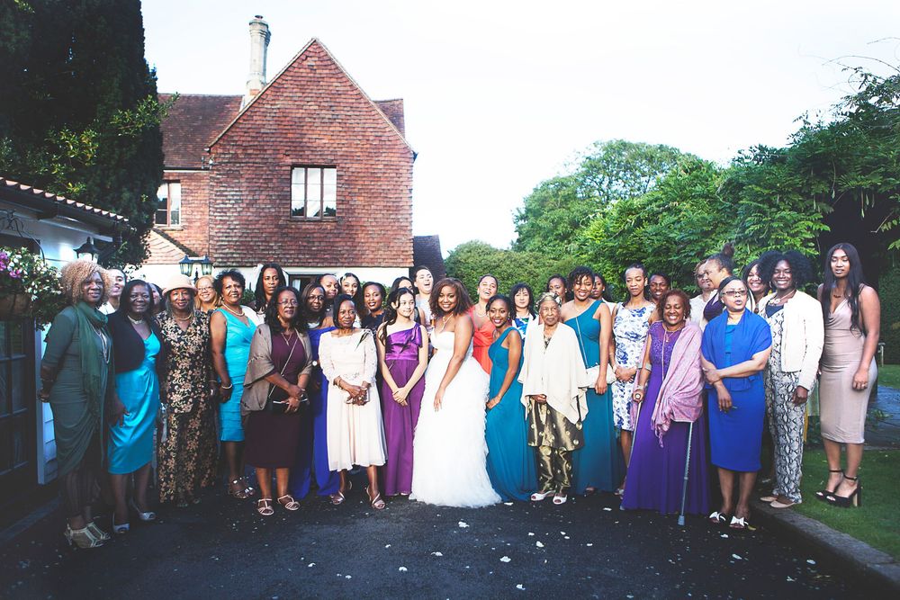 Large group of women in colourfu formal attire posing together outside a brick building at a wedding celebration. At Oaks farm wedding venue