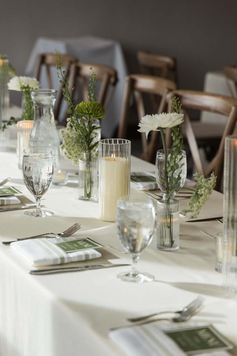Elegant wedding reception table set with white linens, candles, green and white floral arrangements, and crystal glassware.