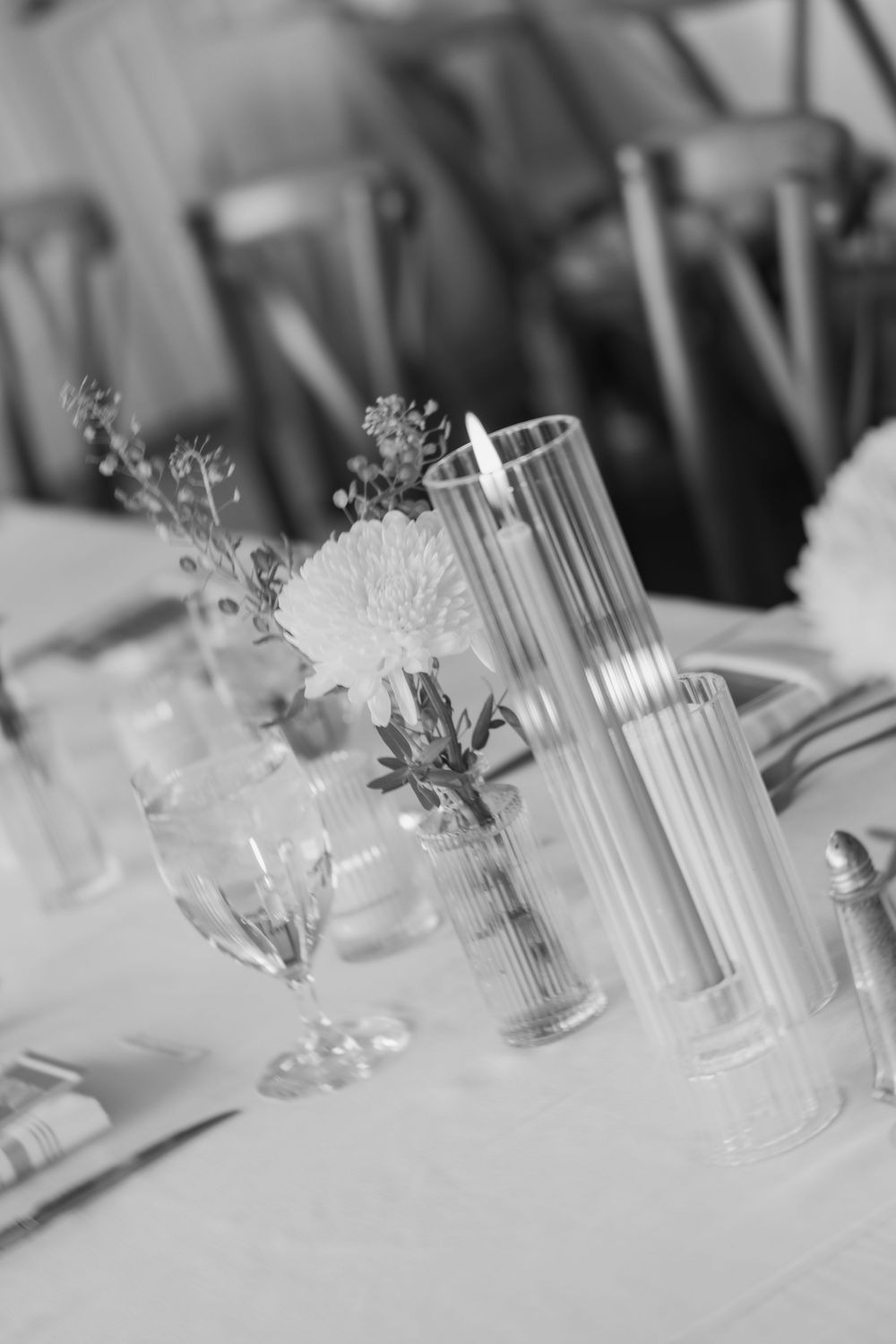 Black and white photo of an elegant table setting with floral arrangements, candle, and glassware for a formal event.