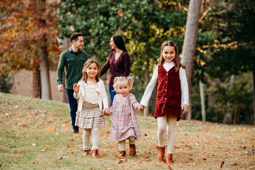 A happy family of five walks together through a park during autumn leaf season.