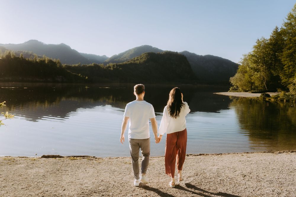 Couple holding hands standing by a calm mountain lake on a sunny day.