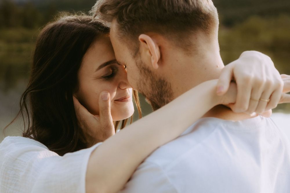 A couple shares a tender almost-kiss moment, the man gently cradling the womans face outdoors.