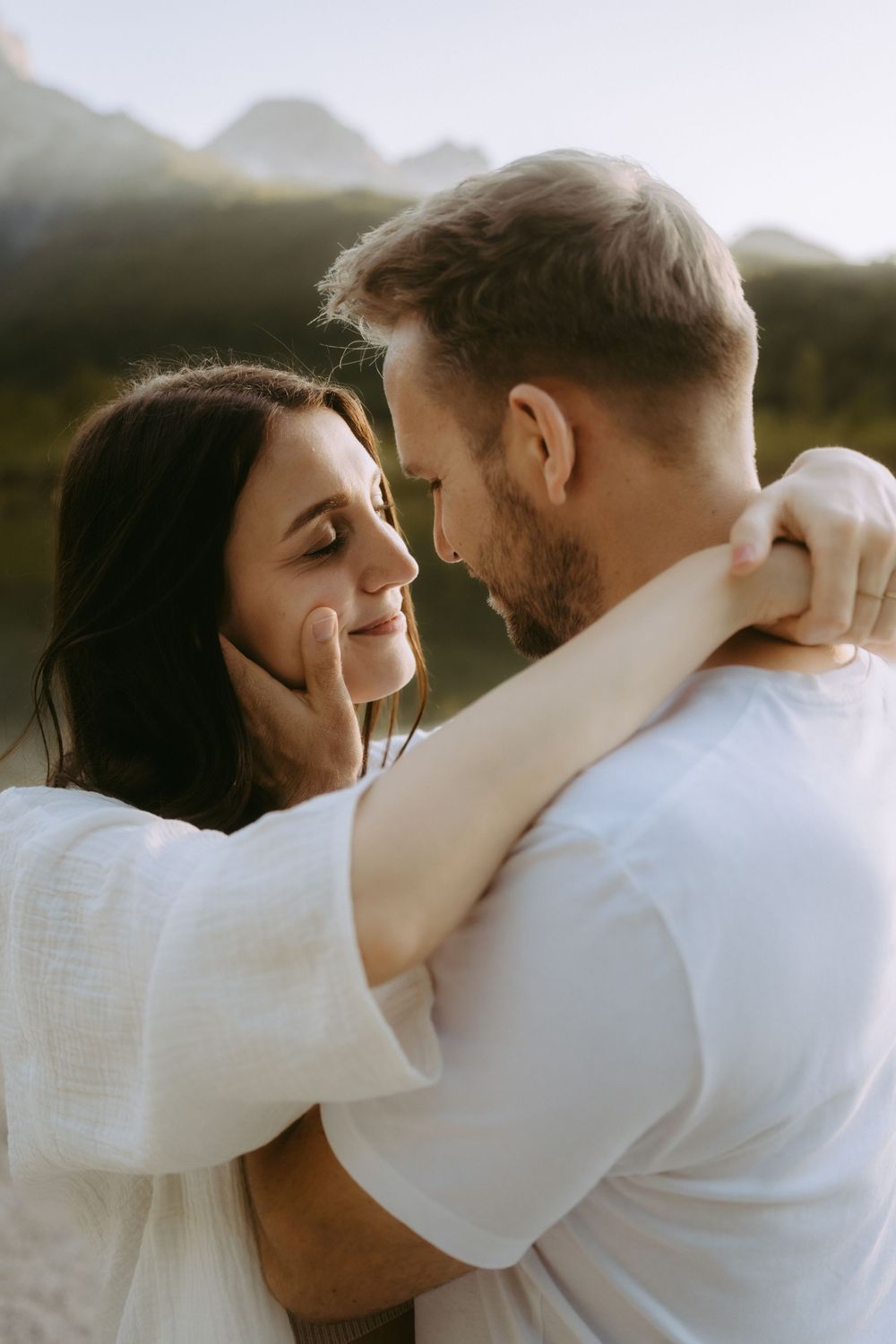 Romantic couple embracing face to face near a mountain lake, man gently cupping womans cheek.