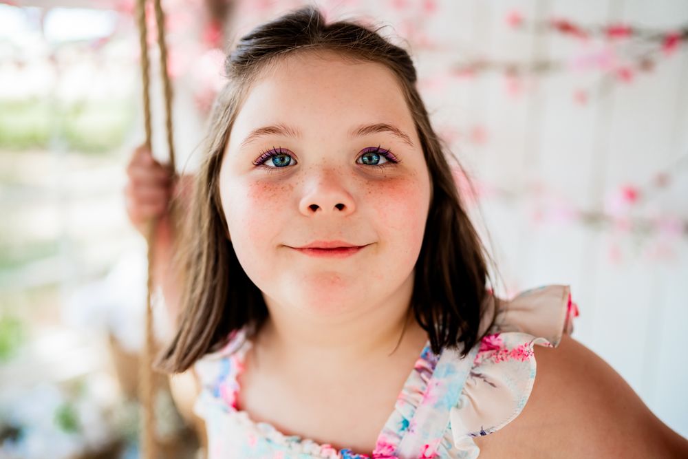 Close-up portrait of a smiling young girl with blue eyes wearing a floral dress on a swing.