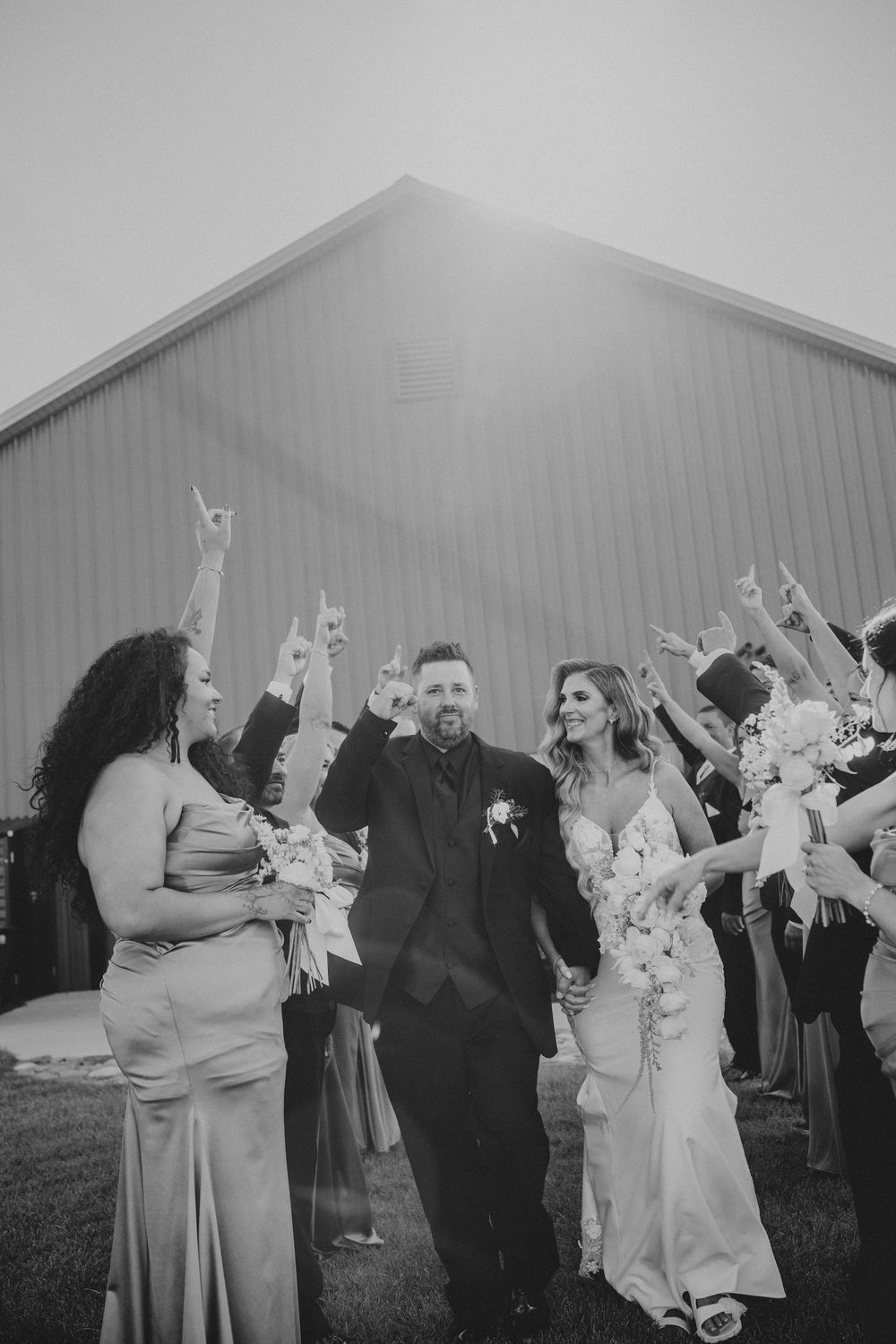 Black and white photo of newlyweds walking through cheering wedding party outside a barn.