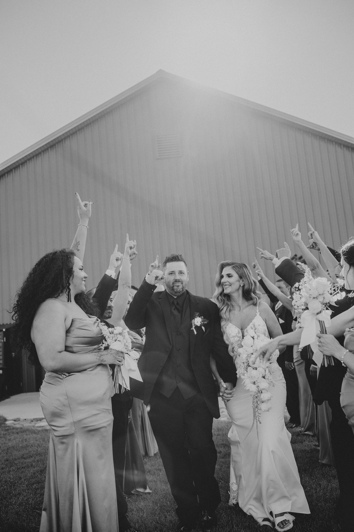 Black and white photo of newlyweds walking through cheering wedding party outside a barn.
