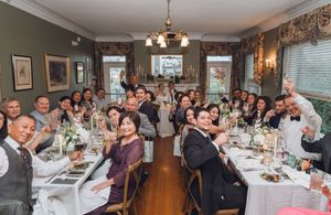 Wedding guests raising glasses in a toast at an elegant indoor reception dinner with candlelit tables.