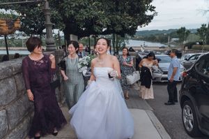 Smiling bride in white gown walking outdoors with wedding guests near a waterfront venue.