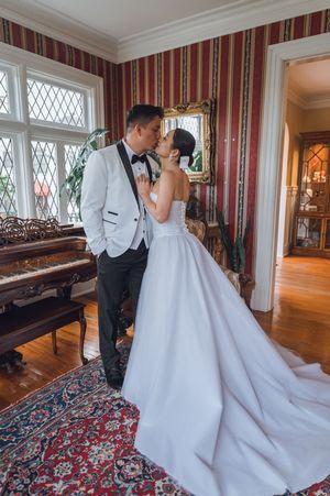 Bride and groom sharing a romantic kiss in a vintage-styled room with striped walls, ornate mirror, and grand piano.