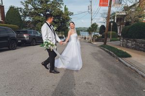 Bride and groom hold hands walking down street near waterfront on wedding day.
