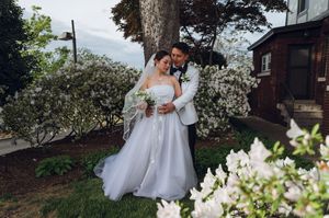 Bride and groom embrace among white flowering bushes in lush garden setting.