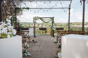 Elegant outdoor wedding ceremony setup with floral arch, string lights, and scenic river views on a stone patio.