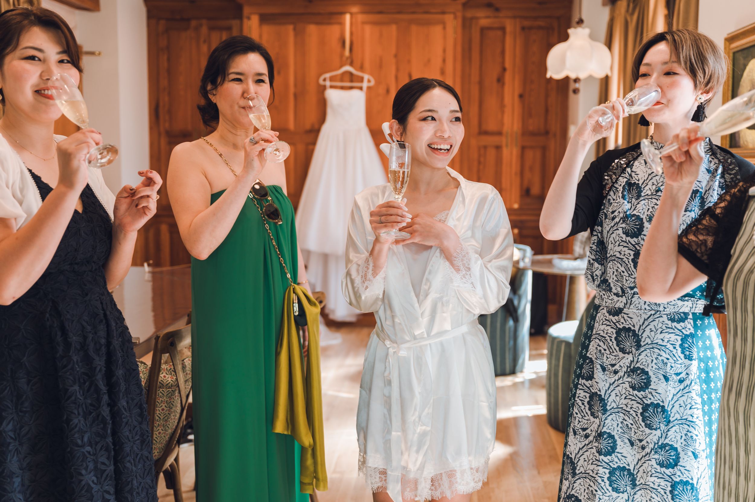 Bridesmaids and bride in robe toasting with champagne flutes during wedding preparations indoors.
