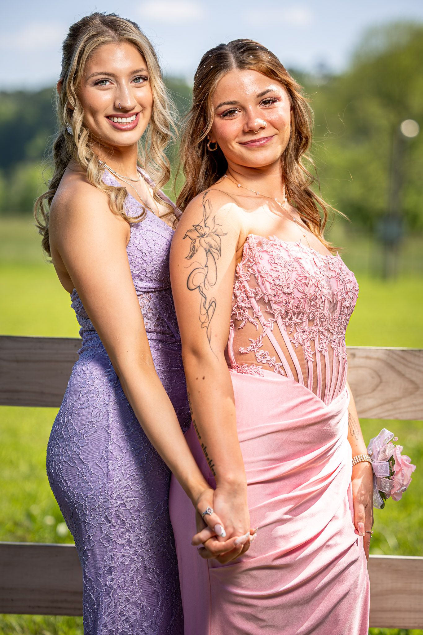 A couple in prom attire poses by a river under a bridge, she in lavender gown, he in dark suit with purple tie.