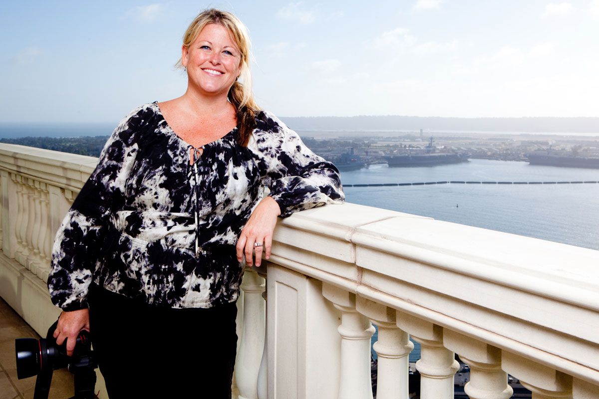 Someone wearing a black and white floral top poses on a balcony overlooking a scenic waterfront view.