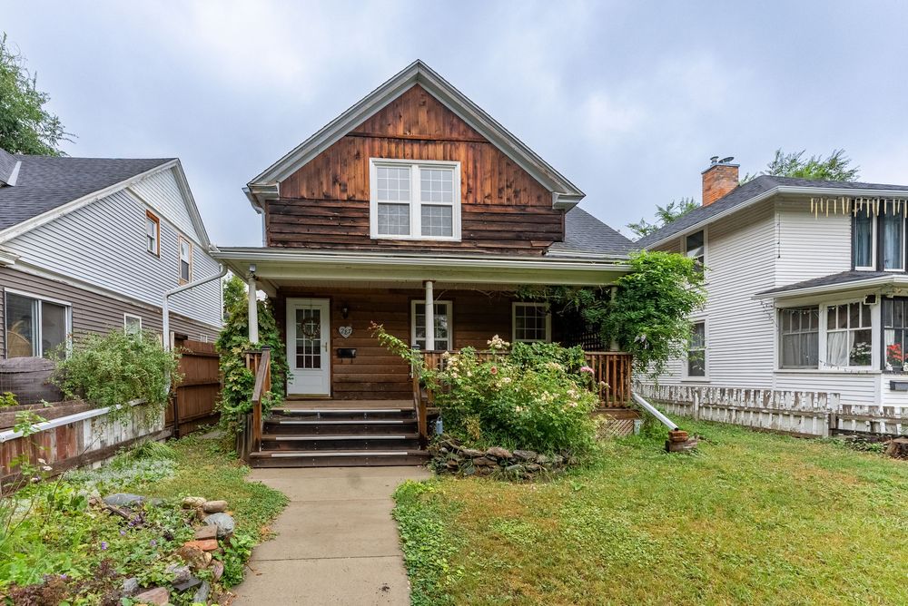 Charming craftsman-style home with cedar shake siding, covered front porch, and lush green lawn in a residential neighborhood.