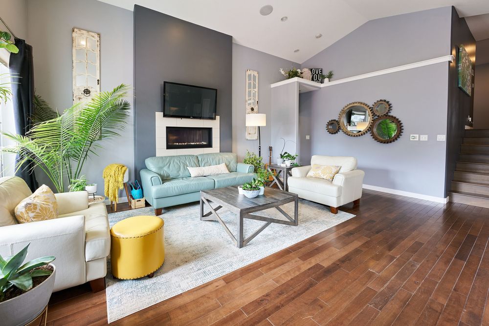 Modern living room with hardwood floors, gray walls, fireplace, teal sofa, and vibrant yellow ottoman accents.