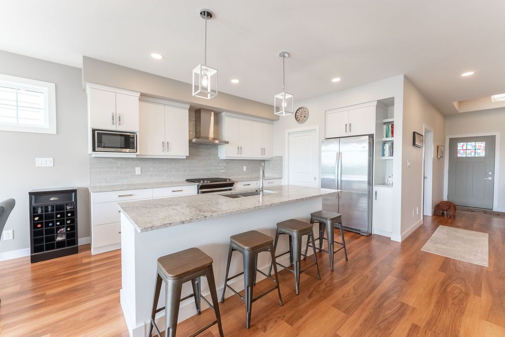Modern open-concept kitchen with white cabinets, granite island, bar stools, stainless appliances, and hardwood floors.