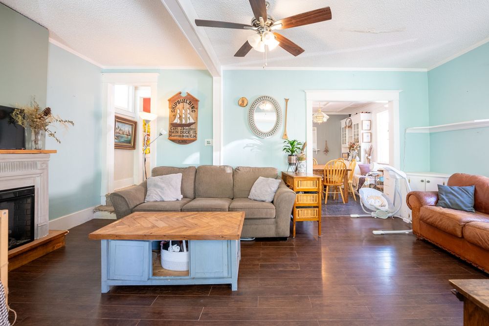 Bright living room with teal walls, hardwood floors, ceiling fan, gray sofa, wooden coffee table, and fireplace.