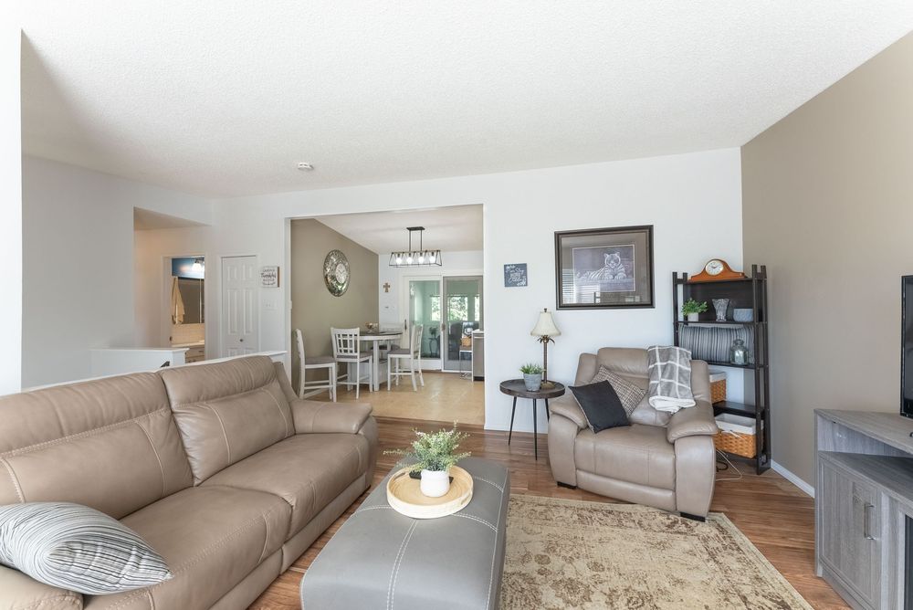 Open-concept living room with tan leather sofa, recliner chair, hardwood floors, and view into dining area with chandelier.
