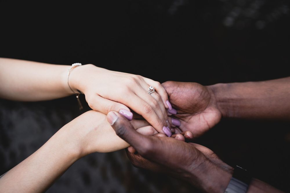 Close-up of interracial couple holding hands showing engagement ring with dark background.