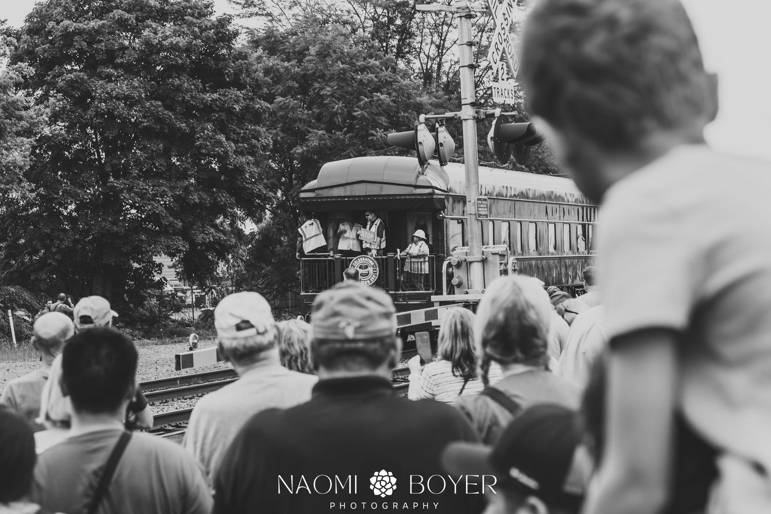 Black and white photo of a crowd watching a vintage steam tractor at an outdoor fair, captured by Naomi Boyer Photography.