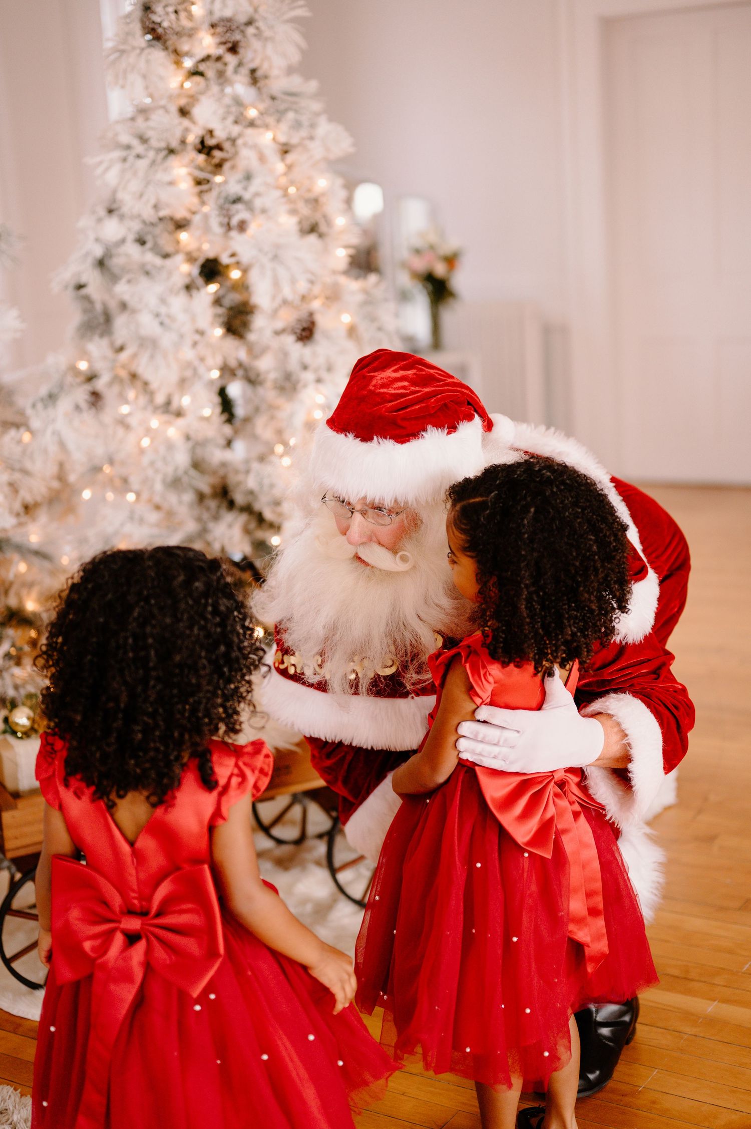 Two girls in red dresses meet Santa Claus beside a white Christmas tree for Cincinnati mini sessions