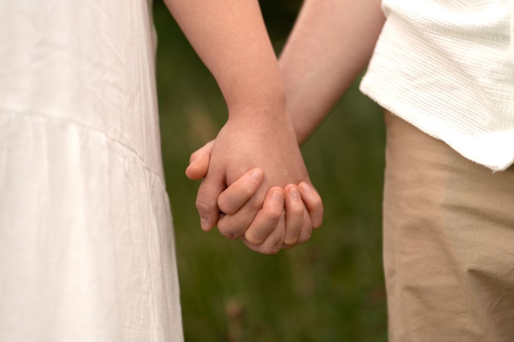 Two children holding hands outdoors, wearing white dress and beige pants, symbolizing friendship and innocence.