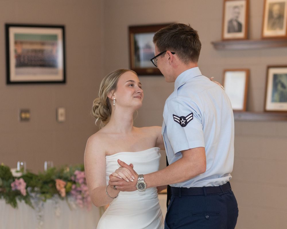 A bride and Air Force groom share their first dance at their wedding reception, gazing lovingly at each other.