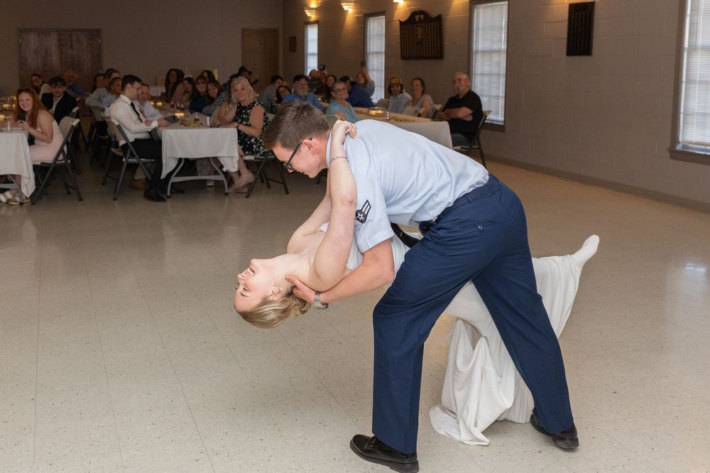 Military groom in uniform dipping bride in white wedding dress during first dance at reception.