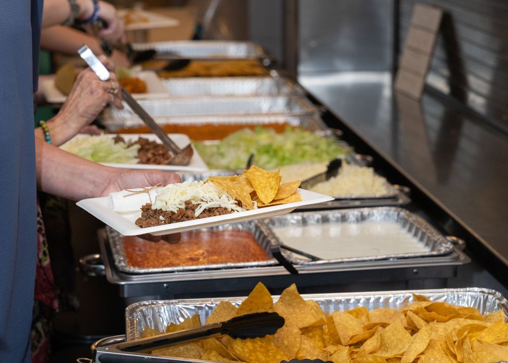 Guests serving themselves from a taco bar buffet with assorted toppings and chips at a catered event.