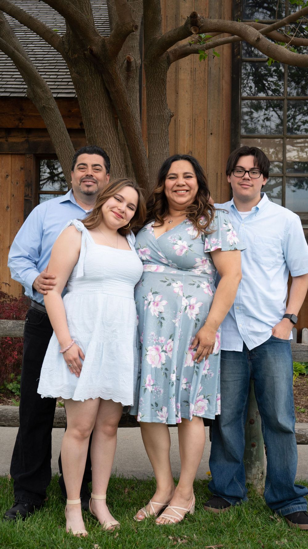Happy family of four posing outdoors, parents with teenage son and daughter in spring clothing.