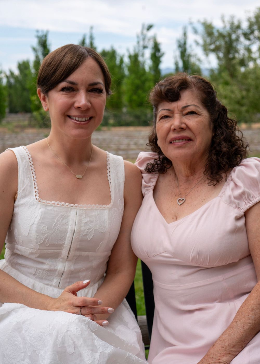Two women in pink and white dresses smiling together outdoors at a garden event.