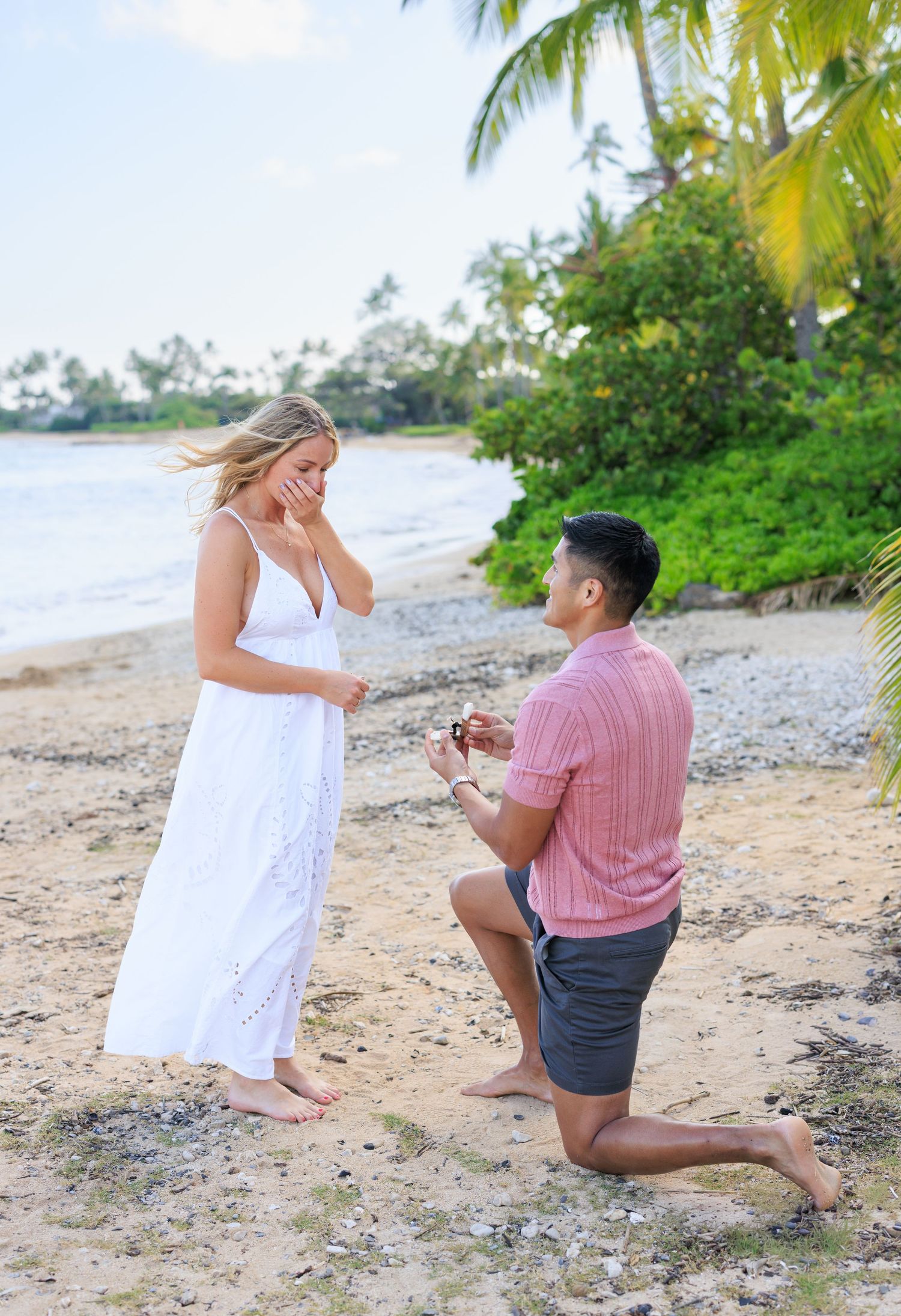 Romantic couple embracing and kissing on a tropical beach with turquoise ocean water in the background.