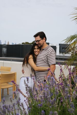 Happy couple embracing and smiling among purple lavender flowers on a rooftop garden.