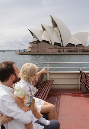 Father and toddler sit on a ferry admiring the Sydney Opera House.