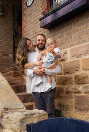 Smiling family of three poses on sandstone steps outside a brick building.