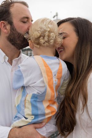 Parents kissing their blond toddler on the cheeks in a heartwarming family portrait outdoors.