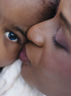 Close-up of a mother kissing her young child with striking blue eyes, capturing a tender moment of love.