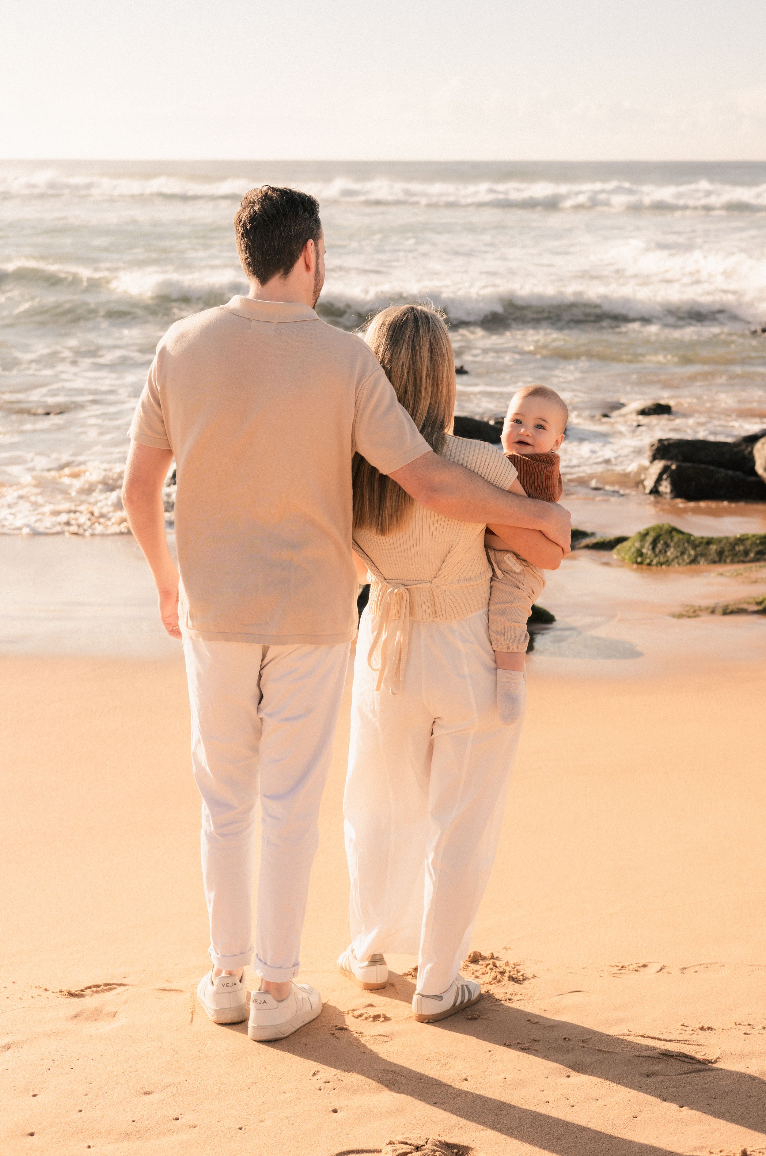 Young family standing together on a sunny beach, parents embracing with their baby.