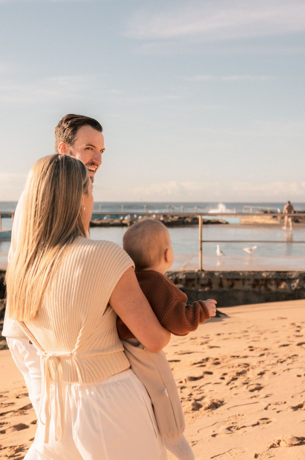 Happy family with baby enjoys a sunny beach day near a ocean pool.