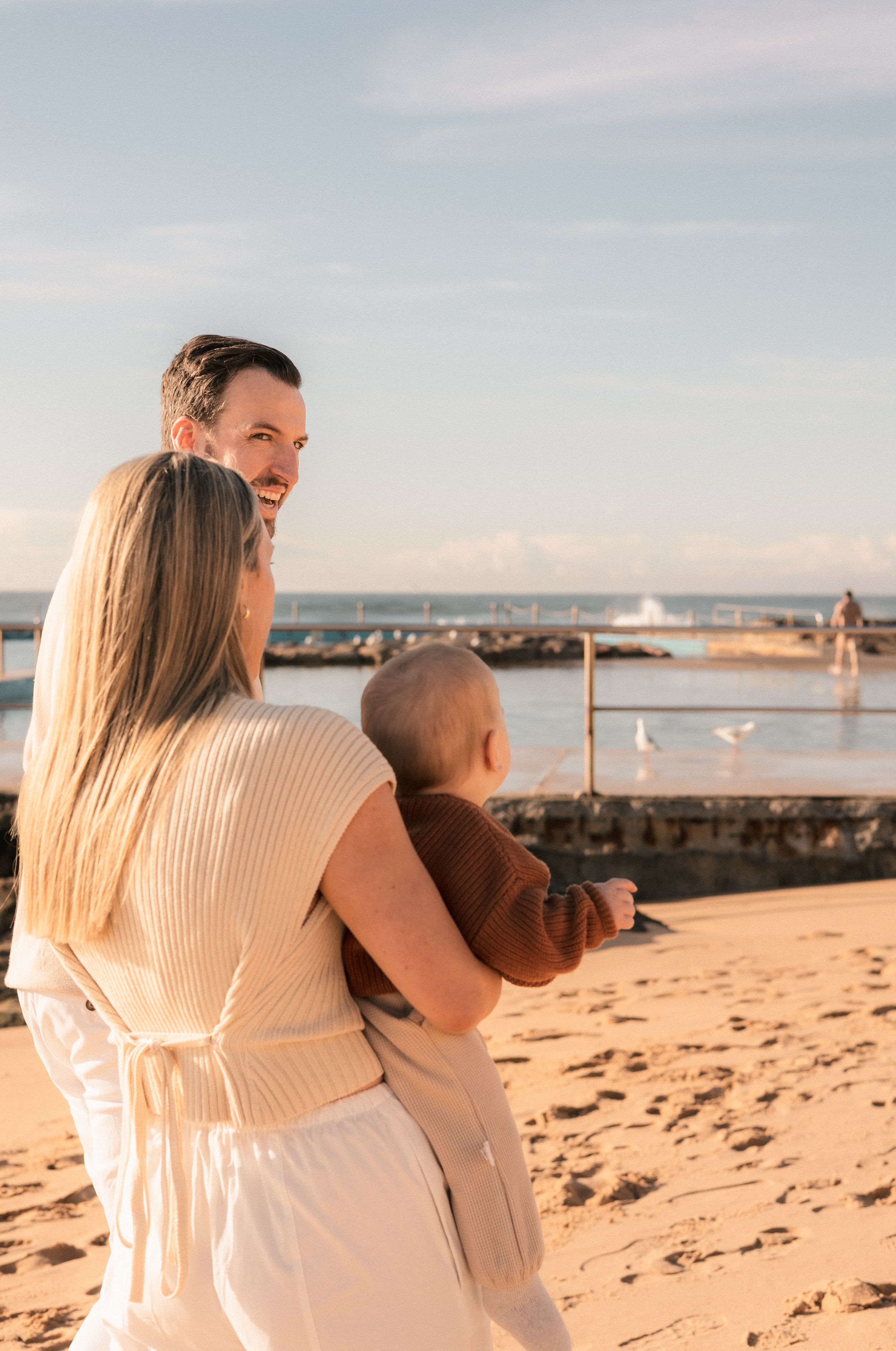 Happy family with baby enjoys a sunny beach day near a ocean pool.