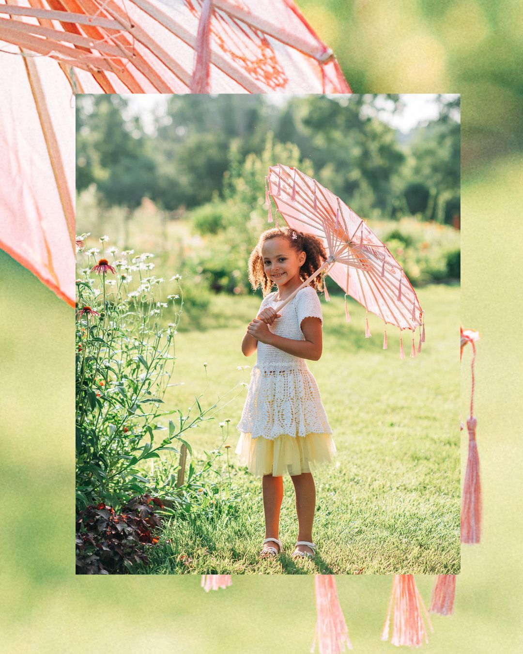 A young girl in a white top and yellow tutu skirt holds a pink parasol umbrella while standing on green grass outdoors.