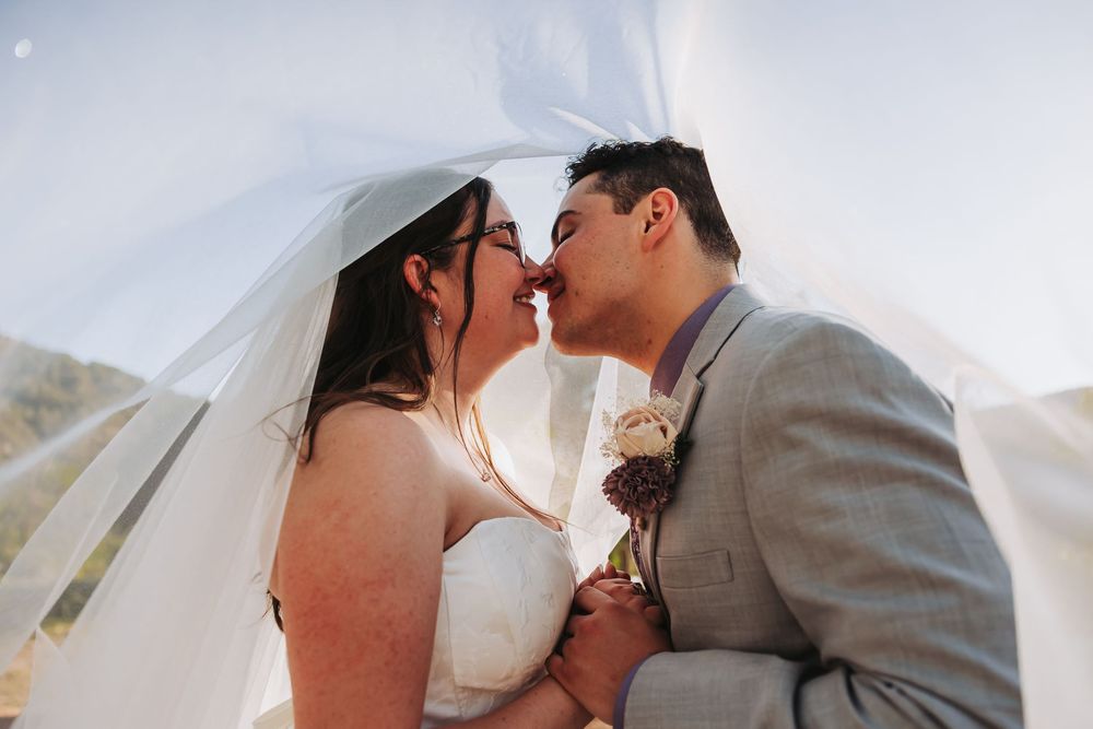 Bride and groom sharing a romantic kiss under a flowing white veil on their wedding day.