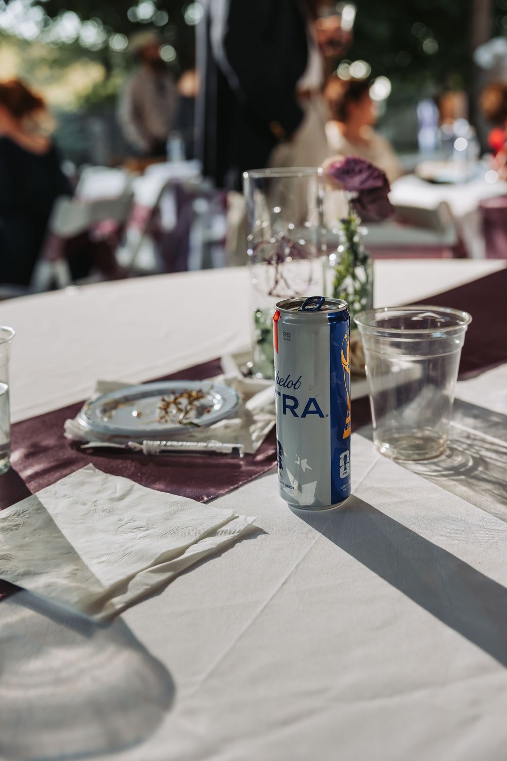 A can of sparkling water on a white tablecloth at an outdoor wedding reception with glasses and floral decor.