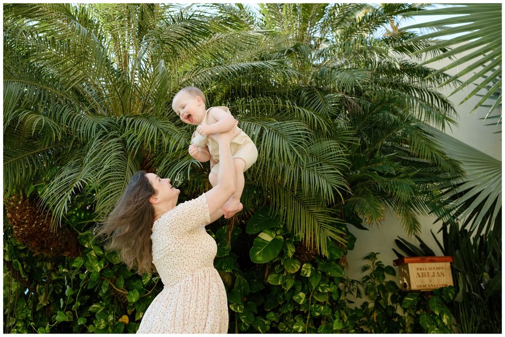 Grand Velas Riviera Nayarit Family Photographer capturing a mother lifting her baby beneath tropical palms during a family photo session.