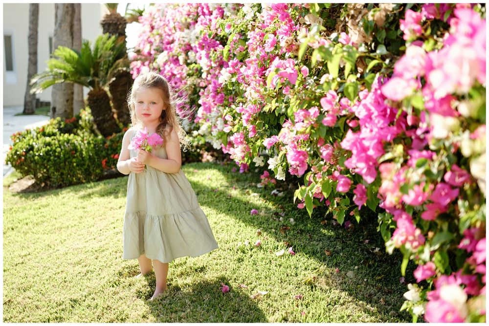 Grand Velas Riviera Nayarit Family Photographer capturing a young girl picking flowers in a sunny garden during candid family photos.