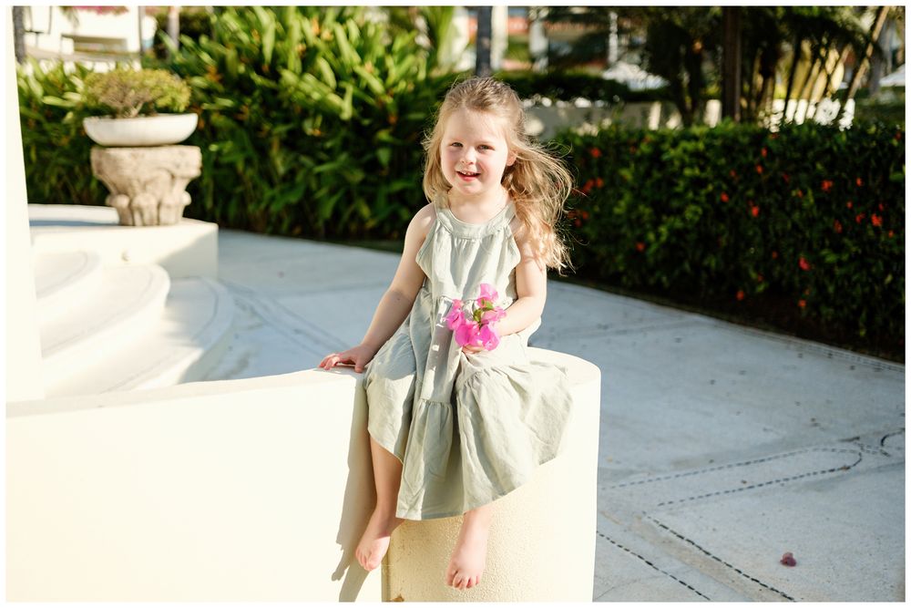 Grand Velas Riviera Nayarit Family Photographer capturing a young girl laughing on a white garden wall during lifestyle family photography.